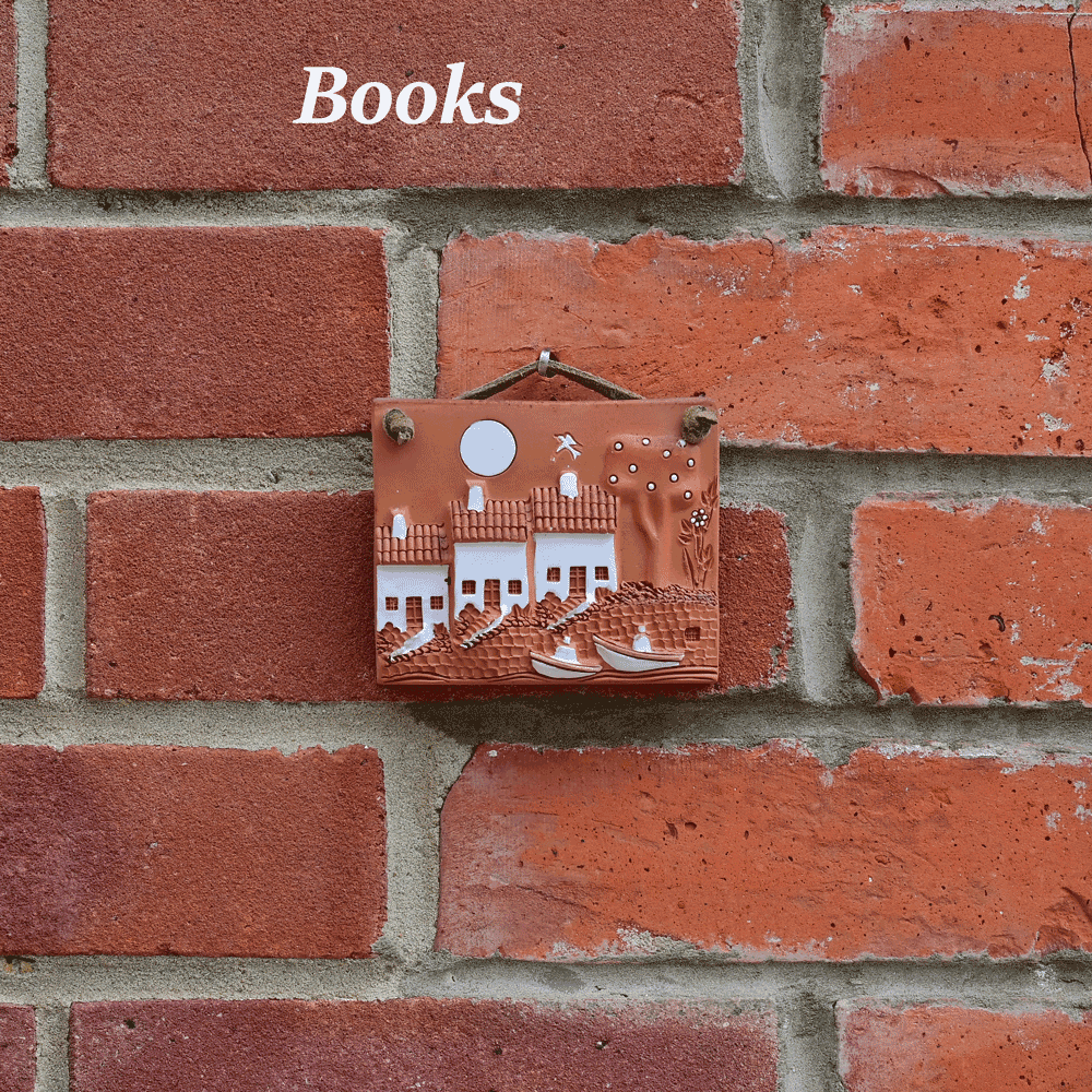 Small hanging terracotta tile with a simple picture of a house against a red brick wall