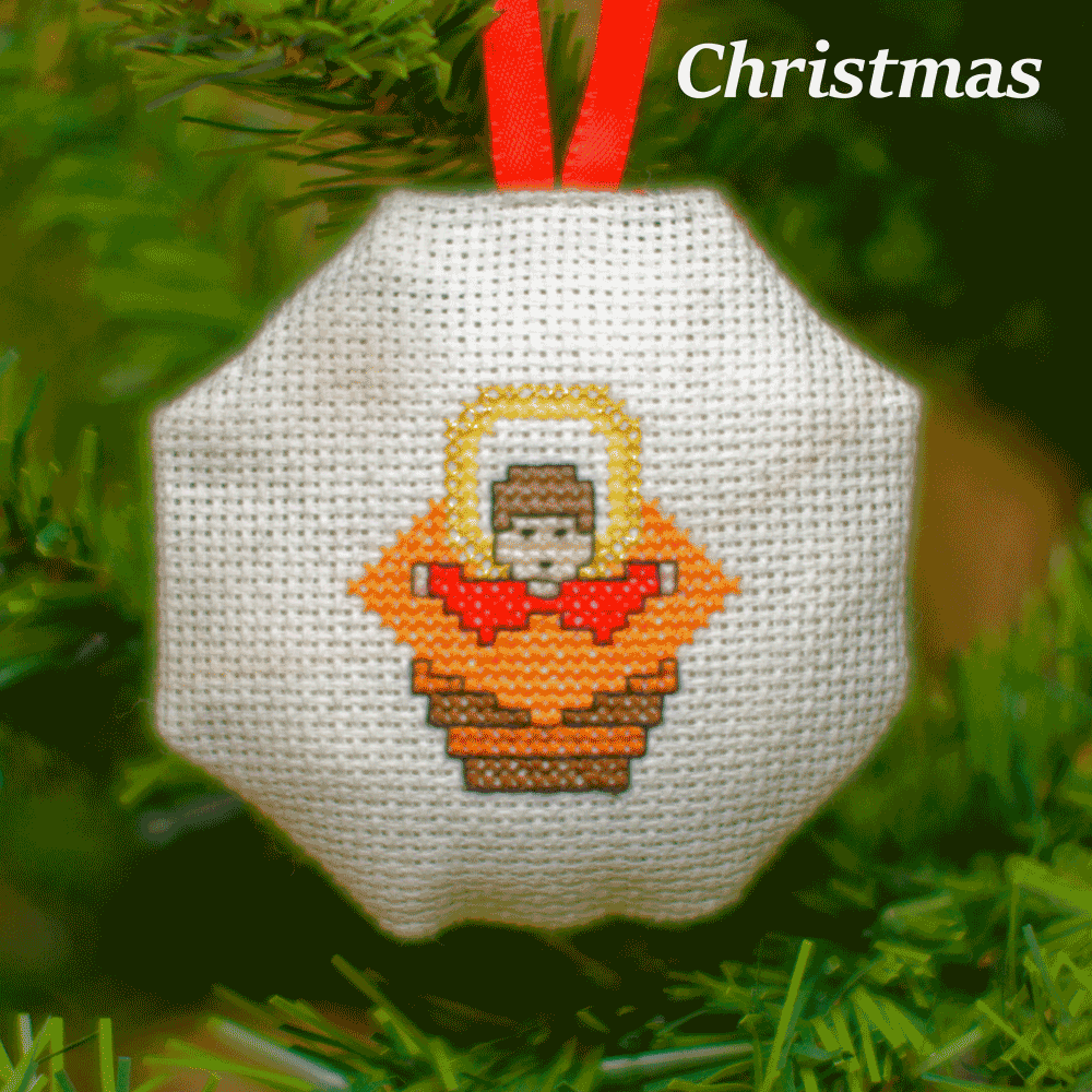 Stitched octagonal picture of a baby in the manger, hanging in a Christmas tree.