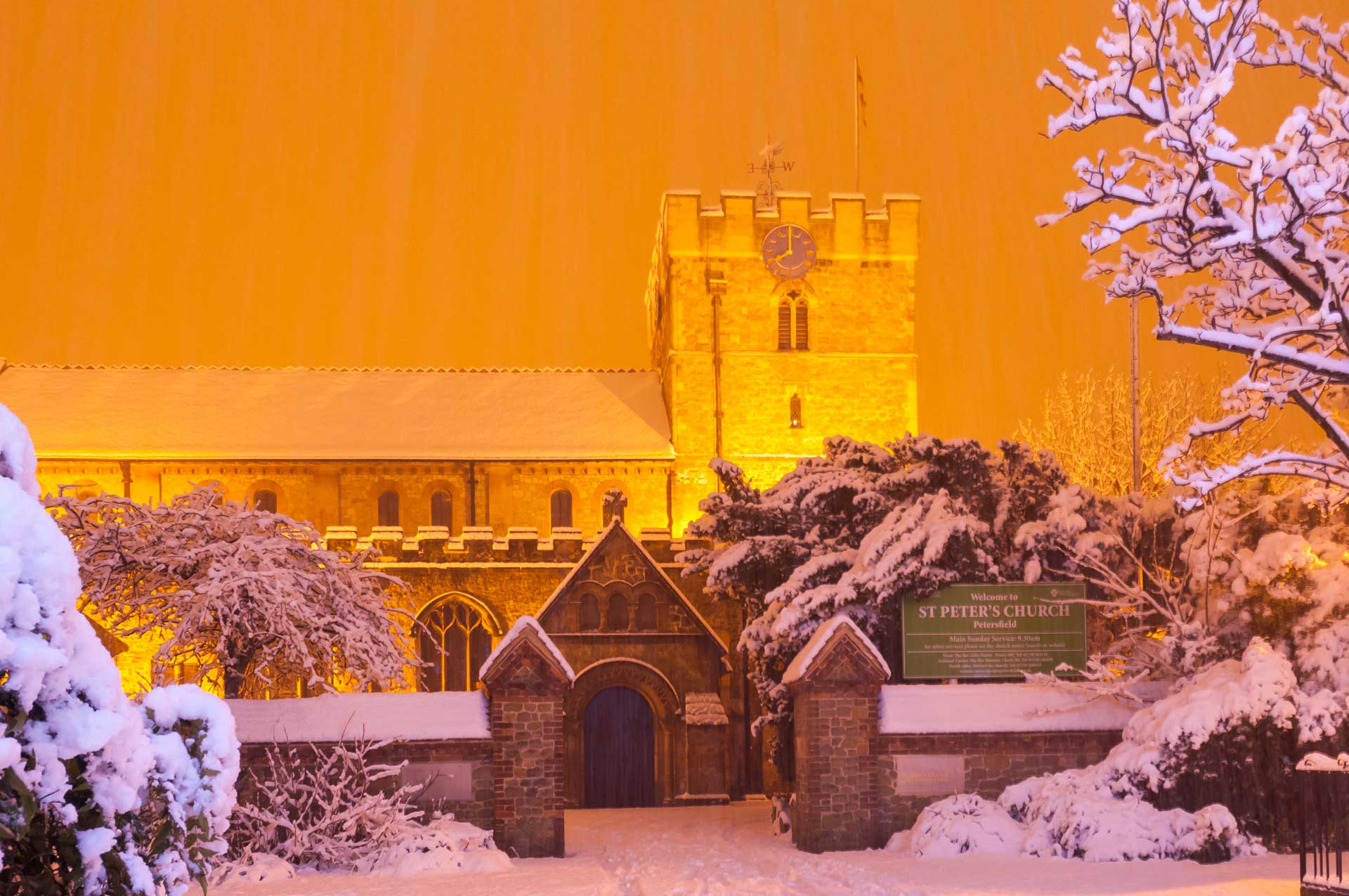 Snowy church at night lit by orange sodium light.