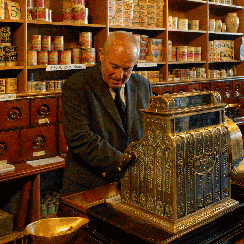 Shop keeper operating an old style brass mechanical cash register (in a living history museum).