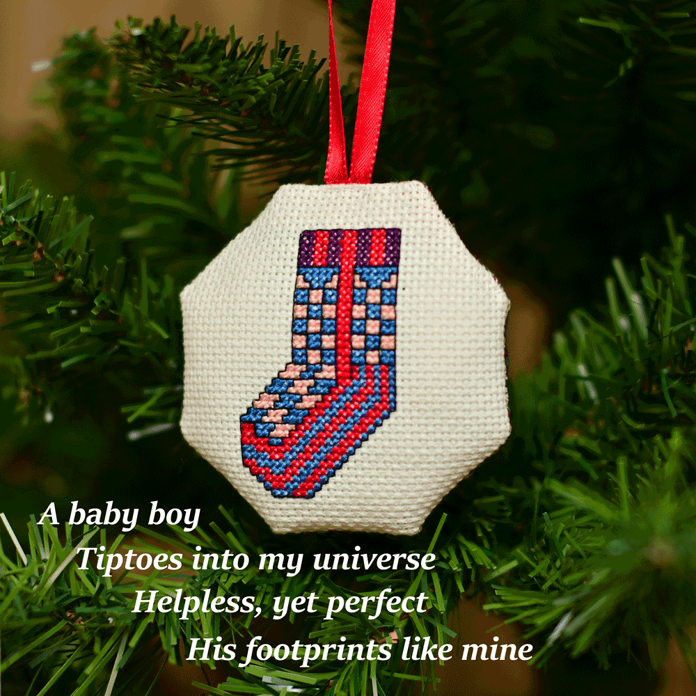 Cross-stitched octagonal picture of a sock, hanging in a Christmas tree.