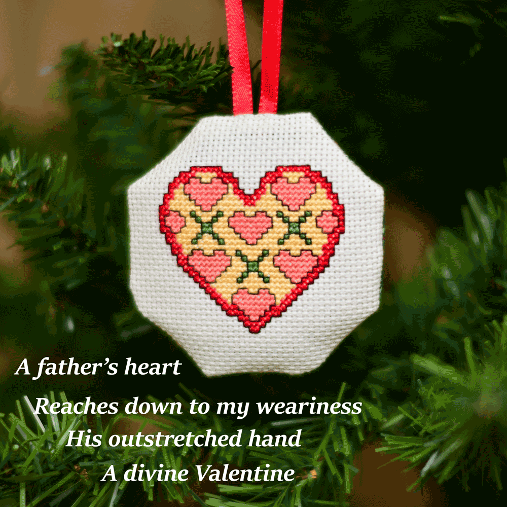 Cross-stitched octagonal picture of a stylised heart shape, hanging in a Christmas tree.