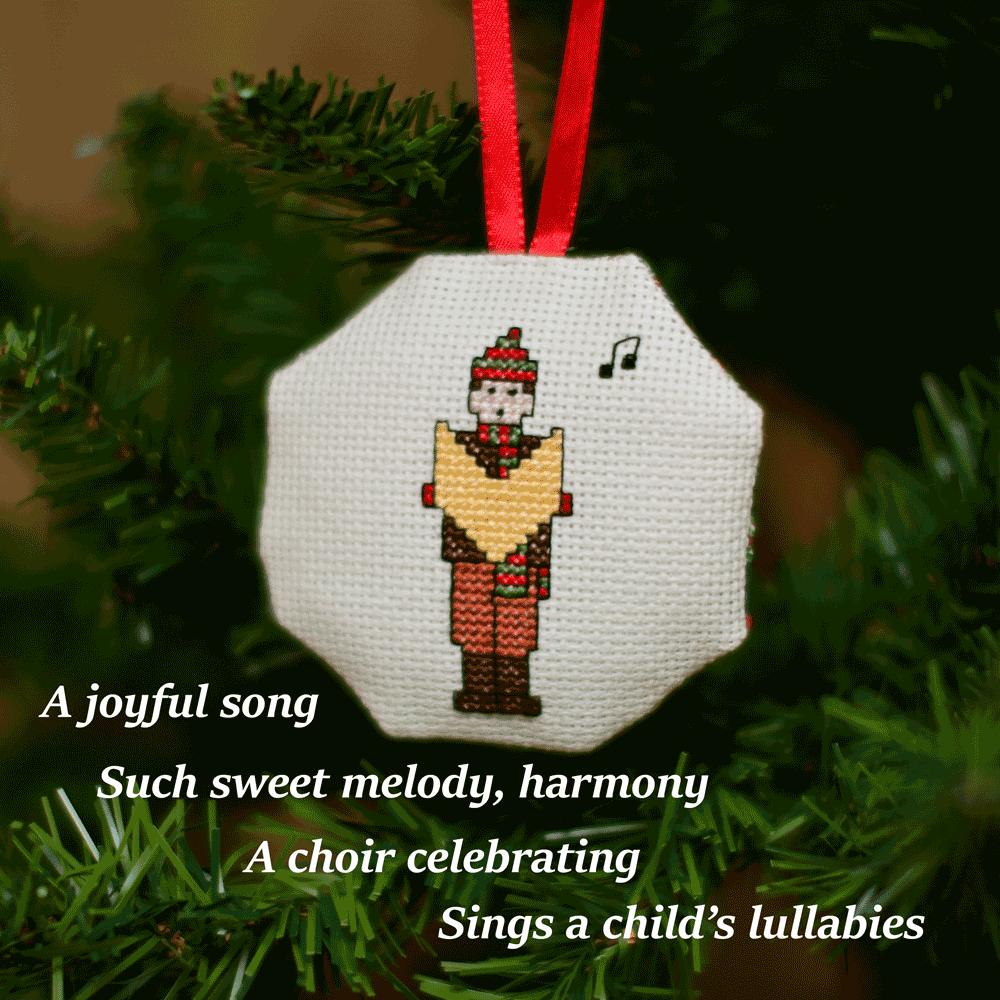 Cross-stitched octagonal picture of a carol singer, hanging in a Christmas tree.