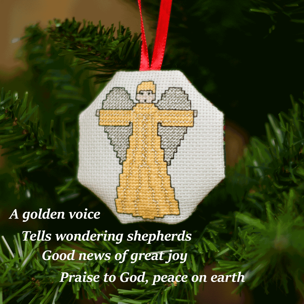 Cross-stitched octagonal picture of a winged angel, hanging in a Christmas tree.