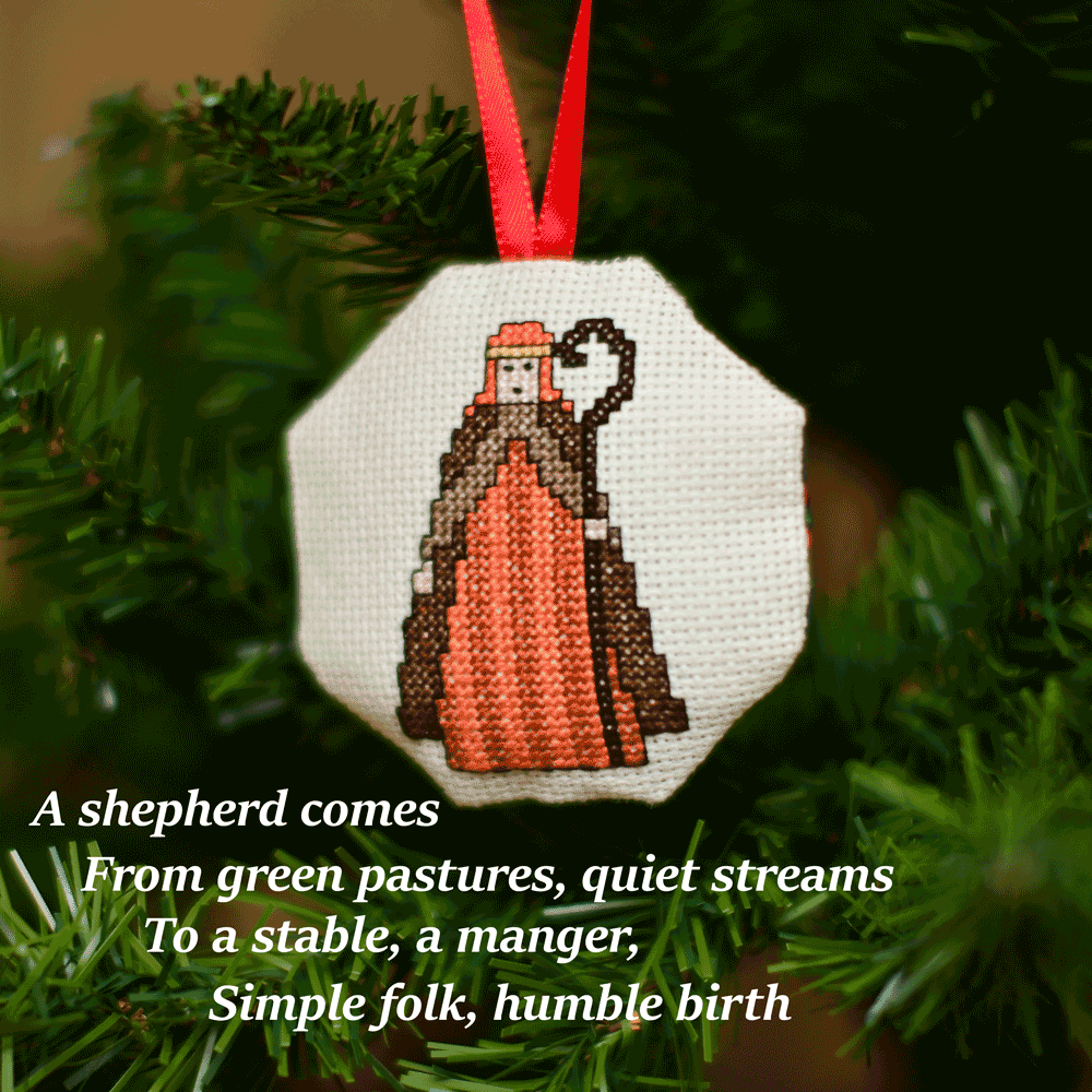Cross-stitched octagonal picture of a shepherd, hanging in a Christmas tree.