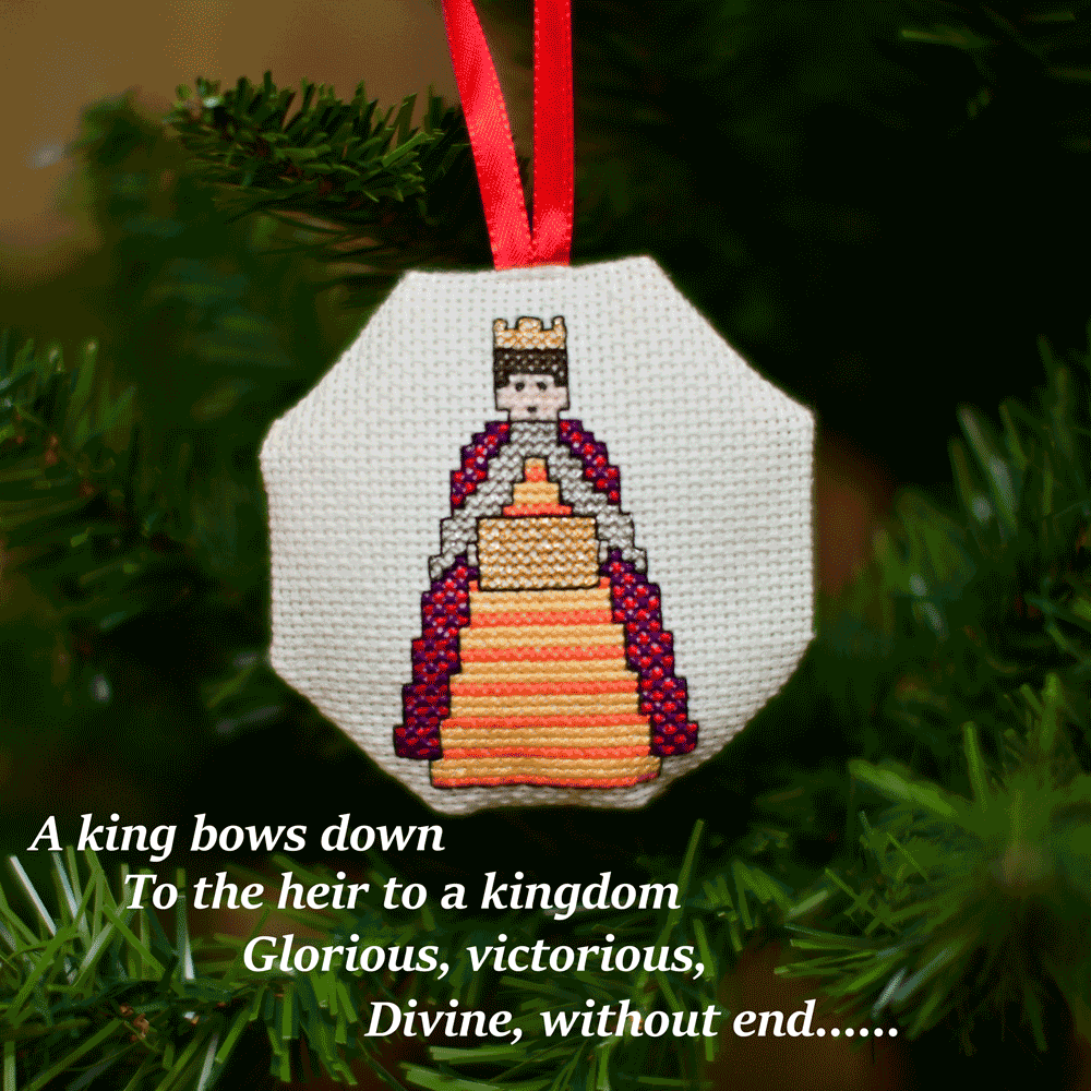 Cross-stitched octagonal picture of a King bearing a gift, hanging in a Christmas tree.